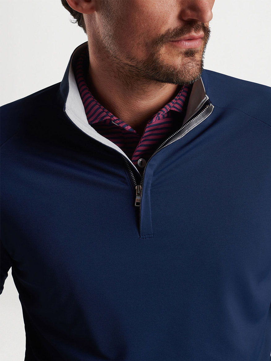 Close-up of a man wearing a Peter Millar Stealth Performance Quarter-Zip in Navy and a patterned collared shirt.