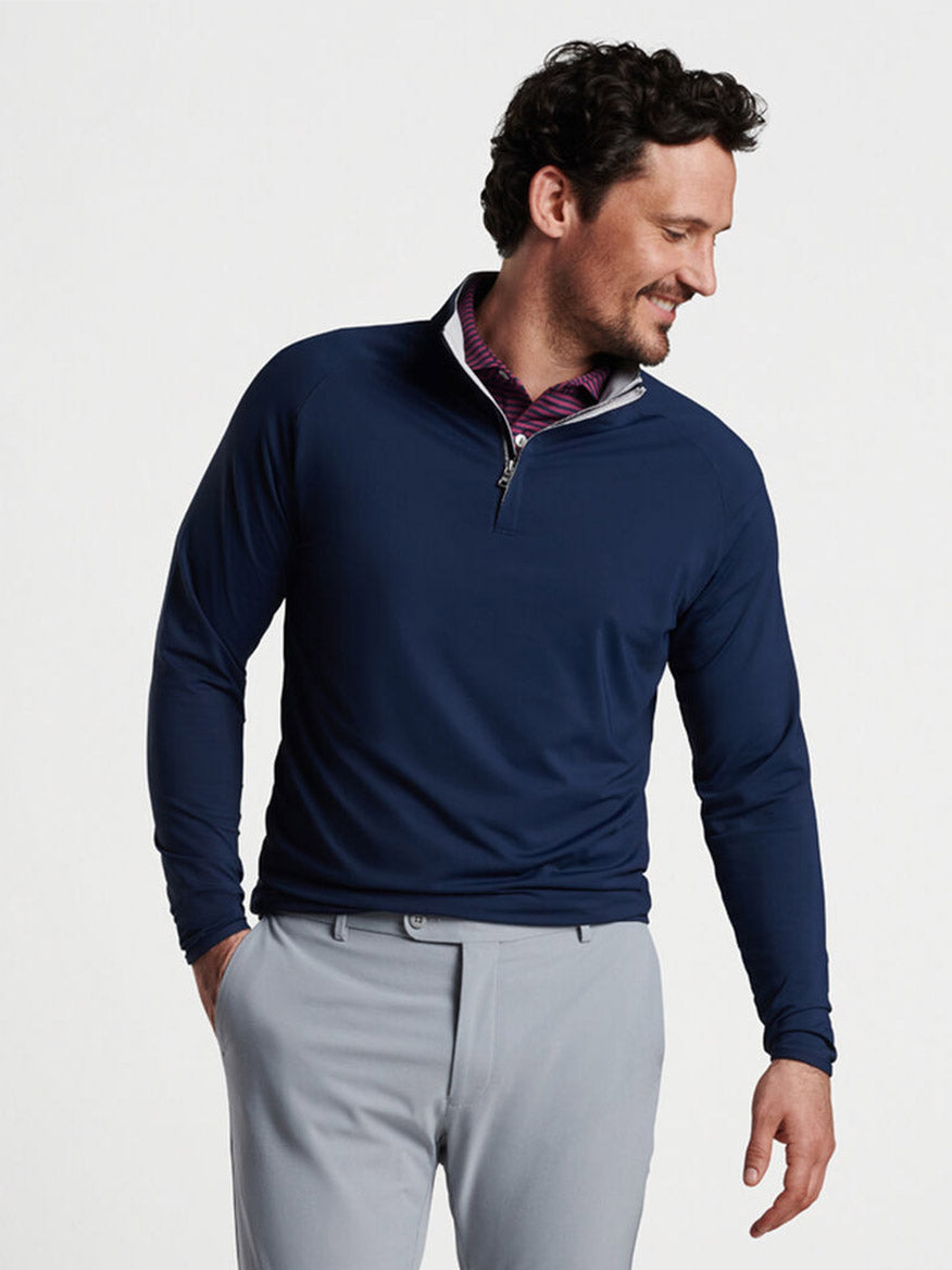 Man in a Peter Millar Stealth Performance Quarter-Zip in Navy and gray pants posing with one hand on his hip.