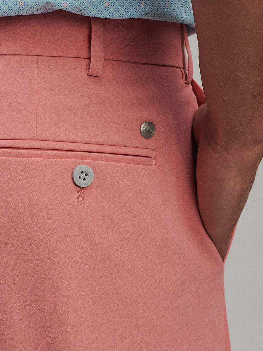 Close-up of a person wearing Peter Millar Surge Performance Short in Pink Crepe featuring four-way stretch, a buttoned back pocket, and a blue patterned shirt tucked in.