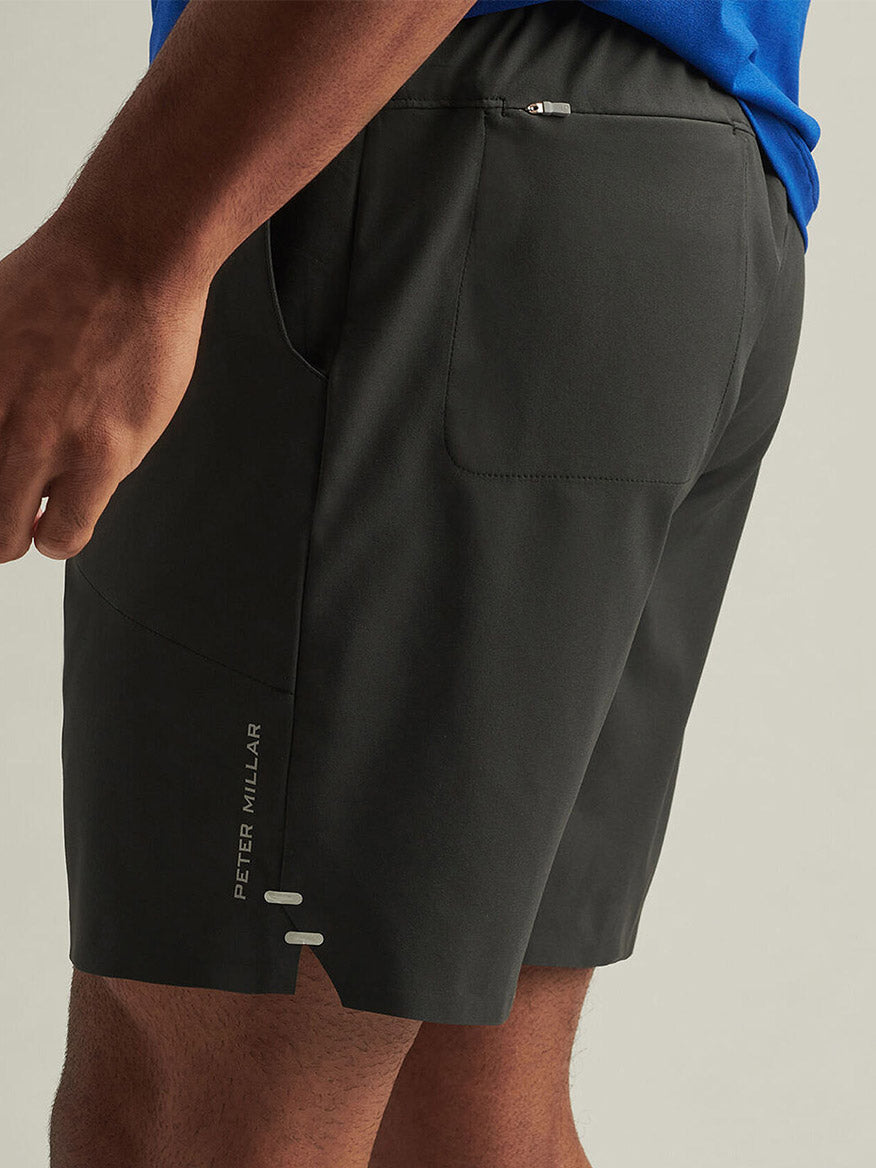 A close-up of a person wearing the Peter Millar Swift Performance Short in Black, made from ultra-lightweight four-way stretch fabric with a back zip pocket, paired with a blue shirt.