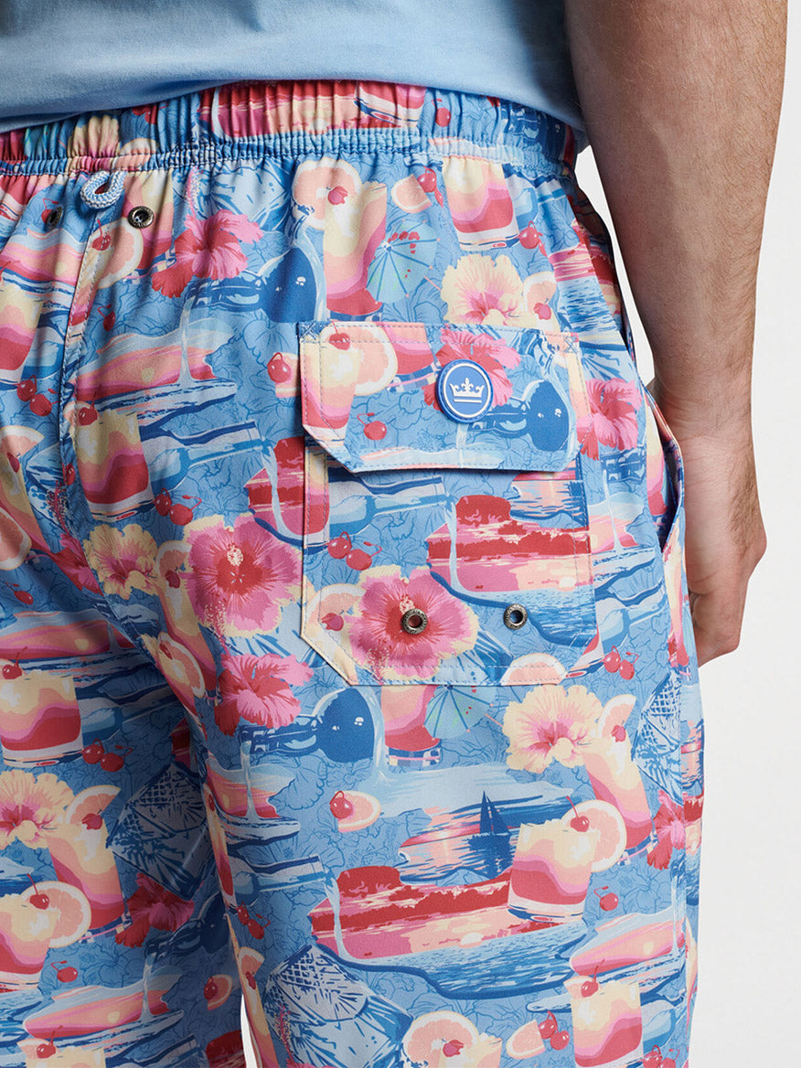 Close-up of a person wearing vibrant floral print Peter Millar Tequila Sunrise swim trunks with pockets.