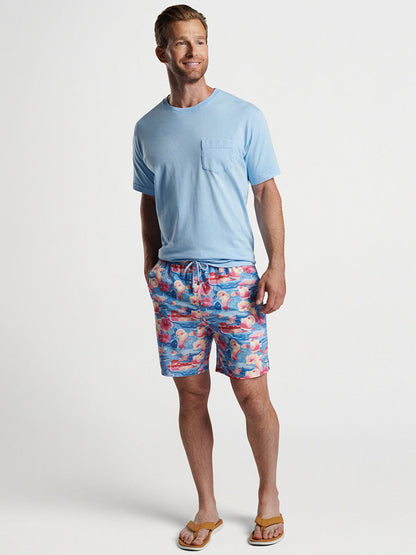 Man posing in light blue t-shirt and wearing Peter Millar Tequila Sunrise Swim Trunk in Infinity with exclusive prints, sporting flip-flops.