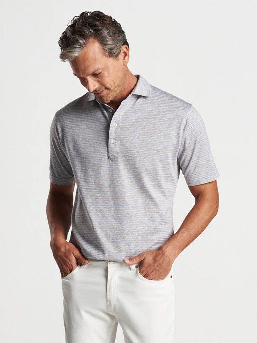 Man in a Peter Millar Tidewater Stripe Polo in British Grey and white pants looking down.
