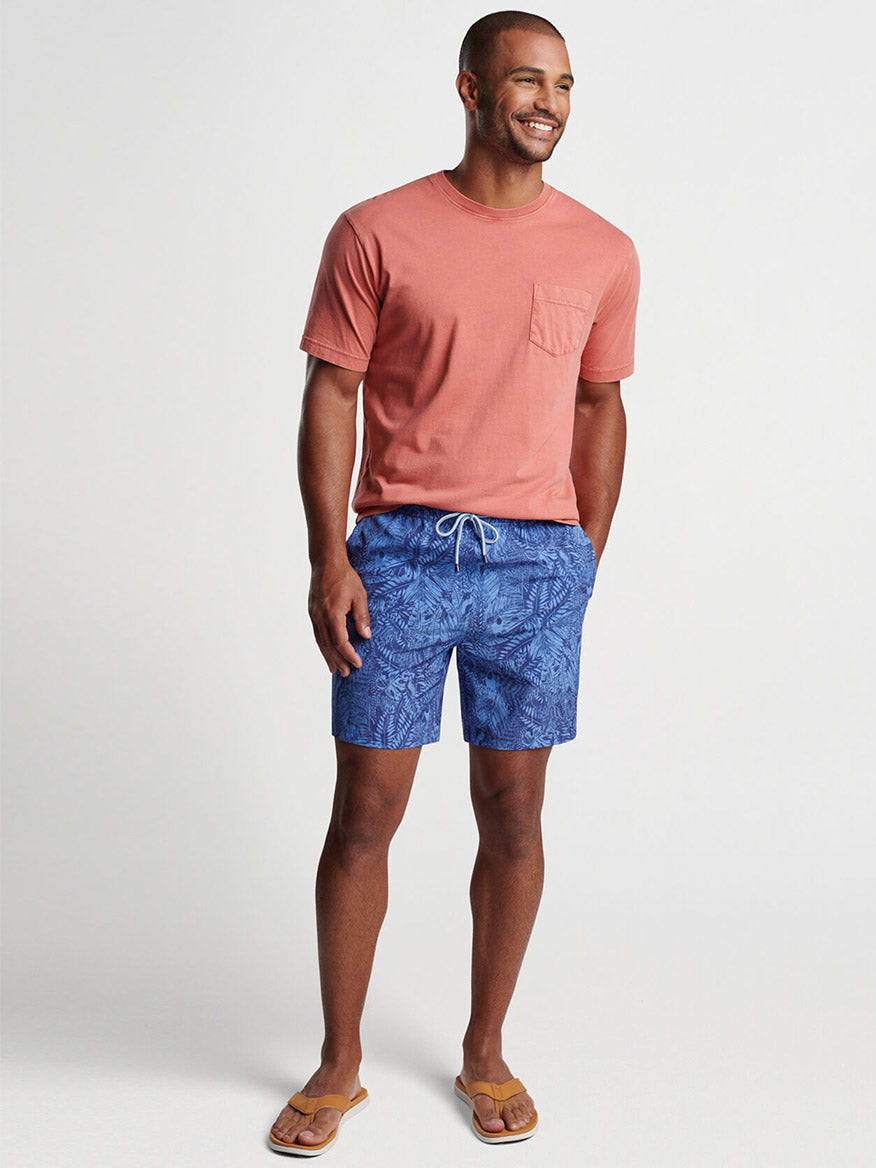 Man smiling while wearing a coral t-shirt and Peter Millar Tropicrazy Swim Trunk in Atlantic Blue, complemented by flip-flops.