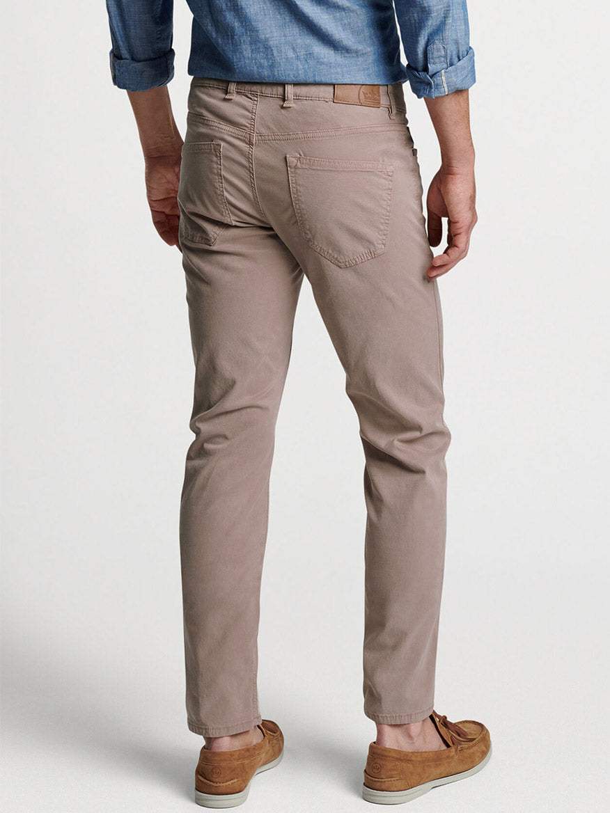 Man wearing Peter Millar Wayfare Five-Pocket Pant in Khaki and a blue shirt, viewed from behind, standing in a neutral pose on a plain background.
