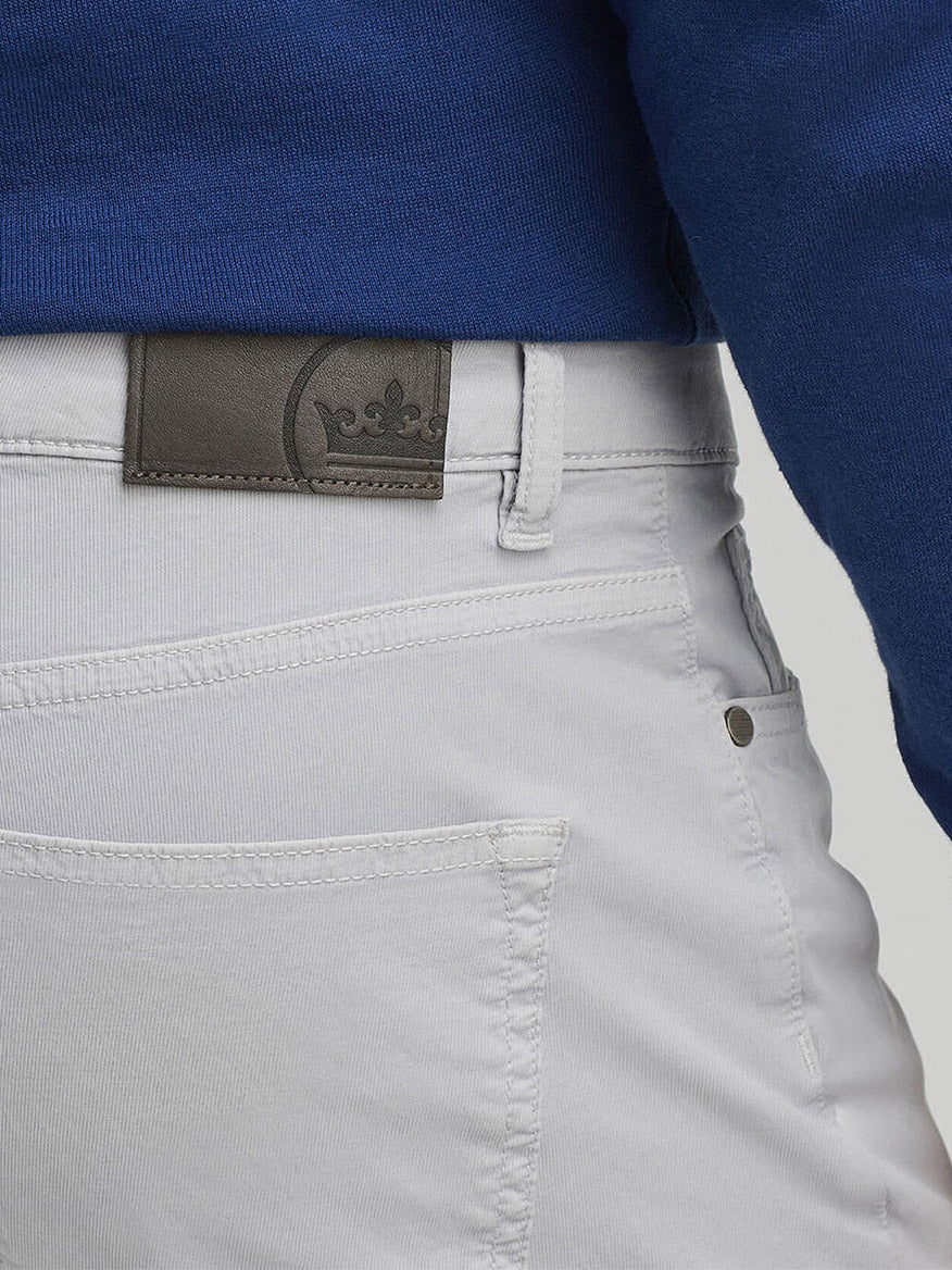 Close-up of a person wearing the Peter Millar Wayfare Five-Pocket Pant in Platinum with a dark belt and blue shirt, highlighting the back pocket and belt loop area.