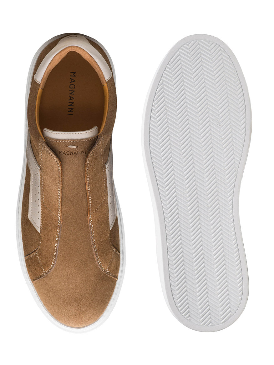 The Magnanni Phoenix Slip in Taupe Suede is a brown slip-on sneaker with a sporty appeal, white sole, and side/bottom view. Perforated details add contemporary style, with the brand visible on the insole.