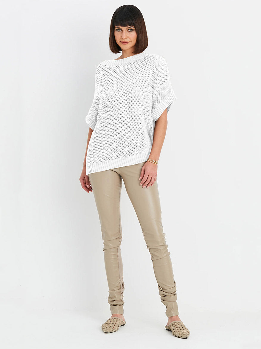 A woman stands against a plain white background wearing the Planet by Lauren G Crochet Popover in White, beige pants, and beige slip-on shoes, radiating effortless bohemian sophistication.