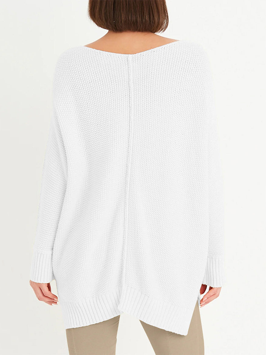 A person is seen from behind wearing a Planet by Lauren G Pebble V-Neck Sweater in white, made from Pima cotton with ribbed cuffs and hem, paired with beige pants against a plain background, exuding relaxed luxury.