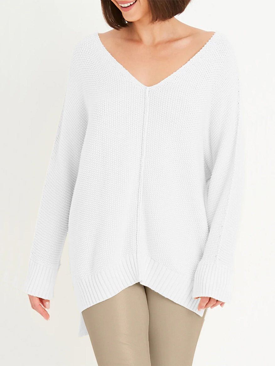 Dressed in the Planet by Lauren G Pebble V-Neck Sweater in White, crafted from soft Pima cotton with a textured knit pattern and long sleeves, they pair it with beige pants. With short brown hair and a warm smile, they embody relaxed luxury and effortless style.