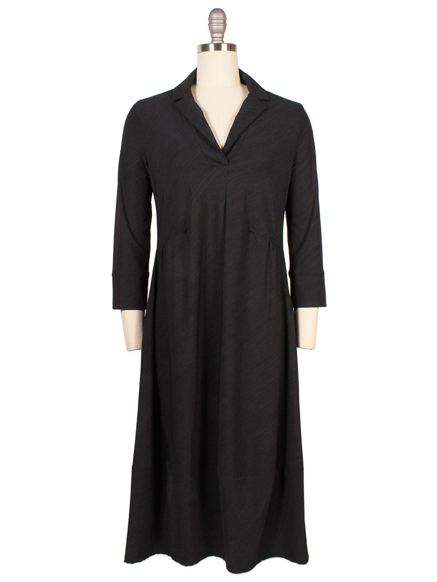 The Porto Flavia Dress in Smoke Reggio is a knee-length, black dress with long sleeves, a split lapel collar, and a slight V-neck, elegantly displayed on a dress form. Made in Italy.