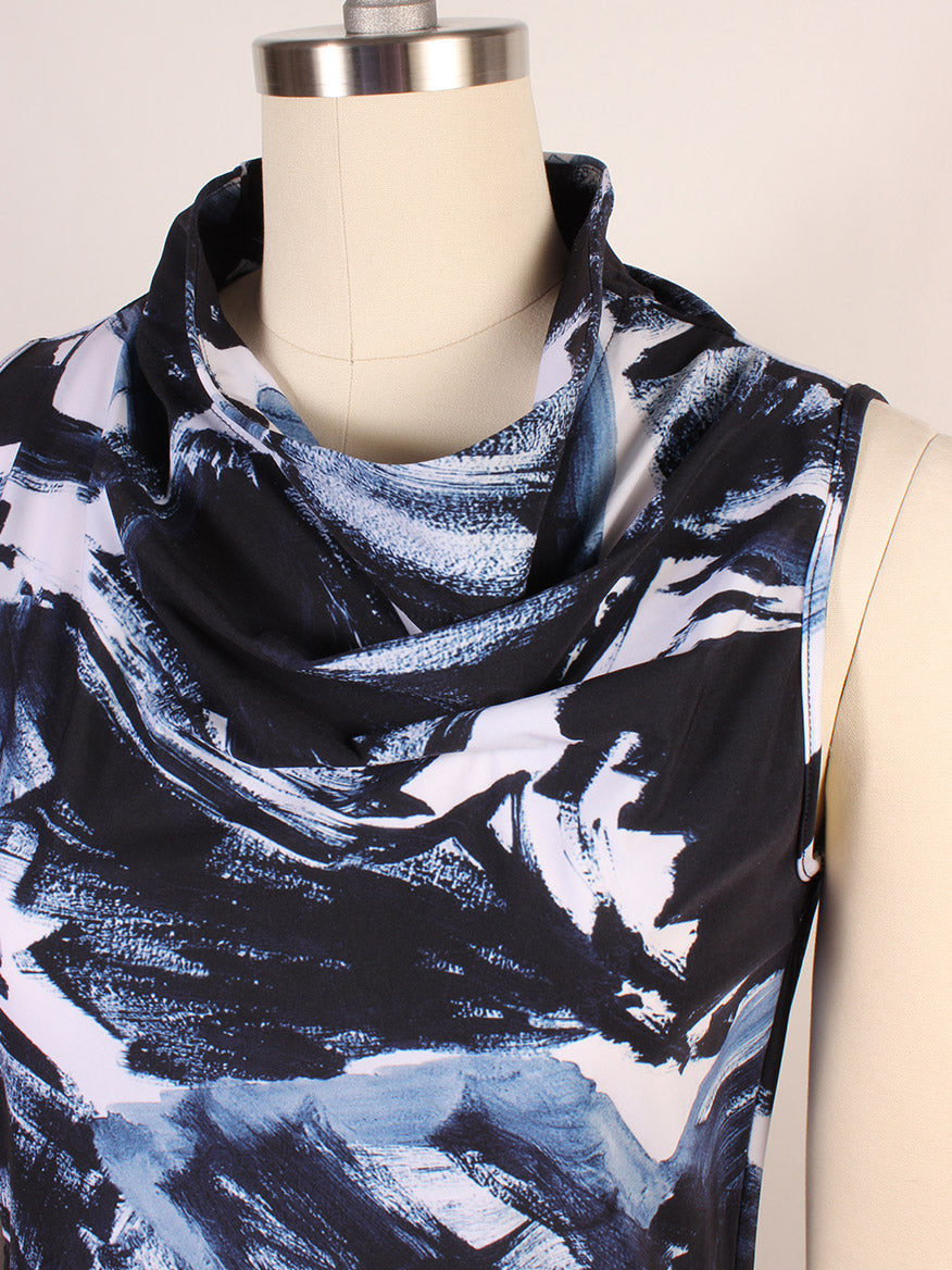 The Porto Indira Ruched Dress in Shadow Shodo features a blue, black, and white abstract brushstroke print with a cowl neckline and ruched sleeveless detailing. Elegantly displayed on a dress form. Made in Italy.