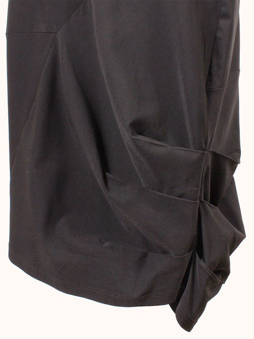 A close-up of the Porto Nomi Sleeveless Dress in Black, showcasing its stretch fabric and gathered draping along one side.