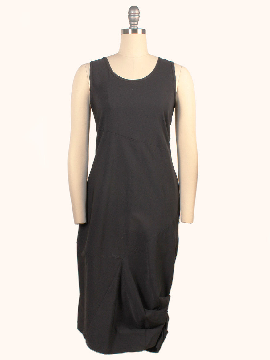 The Porto Nomi Sleeveless Dress in Black is knee-length with a round neckline and asymmetrical gathered detail near the hem. Made in Italy from stretch fabric, it offers a flattering fit and is displayed here on a mannequin.