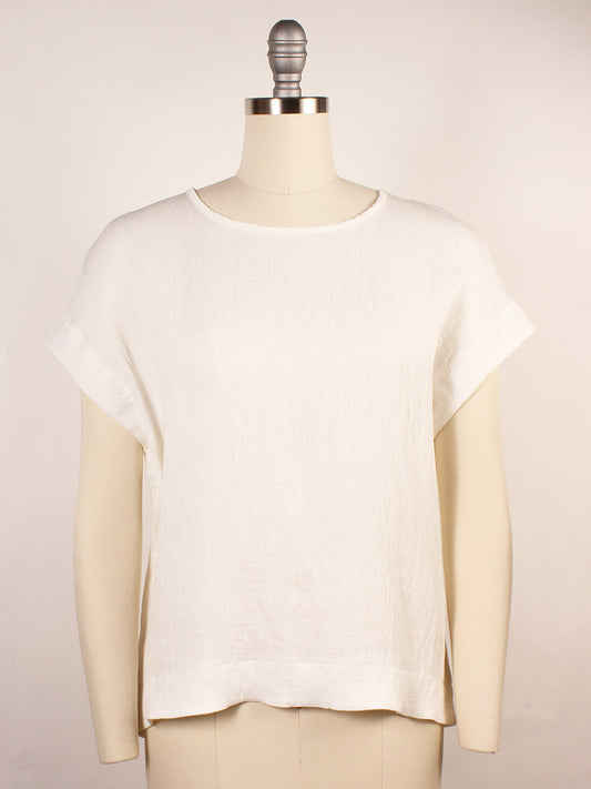 The Porto Sabrina Pleated Top in White, a short-sleeve blouse with a boat neckline and airy Fuji pleat fabric, is showcased on a dress form against a plain background.