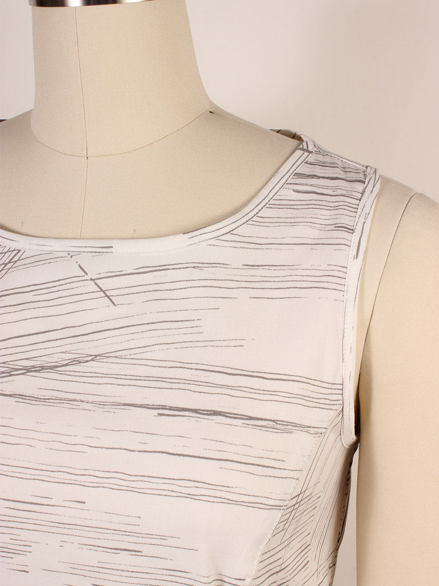 Close-up of the Porto Santiago Sleeveless Dress in Quail Laguna on a mannequin, featuring a boat neckline and light fabric with thin, irregular, horizontal gray lines. Made in Italy.