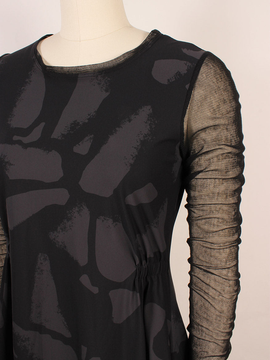 A close-up of a mannequin wearing the Porto Venetian Dress in Smoke Palermo, featuring black abstract patterns and sheer mesh long sleeves, made in Italy.