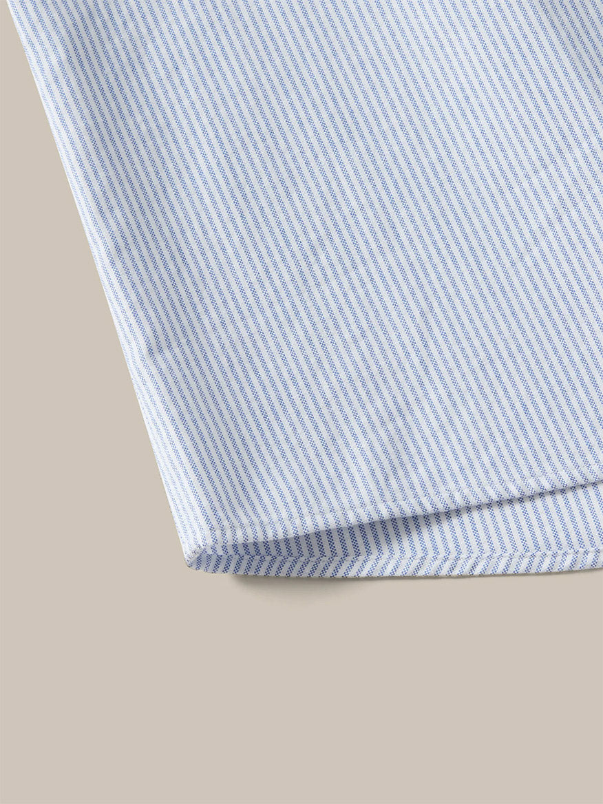 Close-up of the Robert Talbott Harrison Button Down Fun Stripe Oxford Shirt in Navy, Aqua, and Pink, with its colorful striped cotton fabric folded neatly on a beige surface.