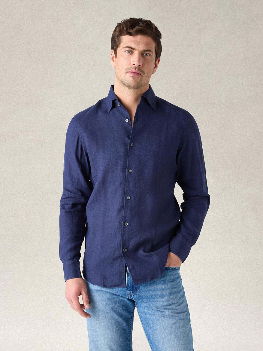 A man wearing the Robert Talbott Morgan Linen Shirt in Navy and light blue jeans stands against a neutral background with one hand in his pocket.