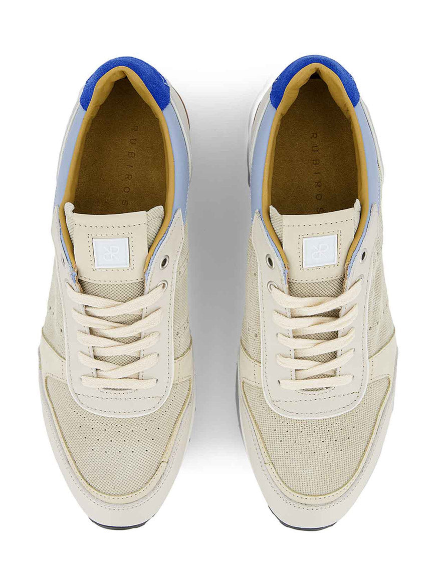 The Rubirosa JOAN Sneakers in Beige feature handcrafted Italian design, white soles, blue heel accents, and perforated detailing, shown from a top-down view.