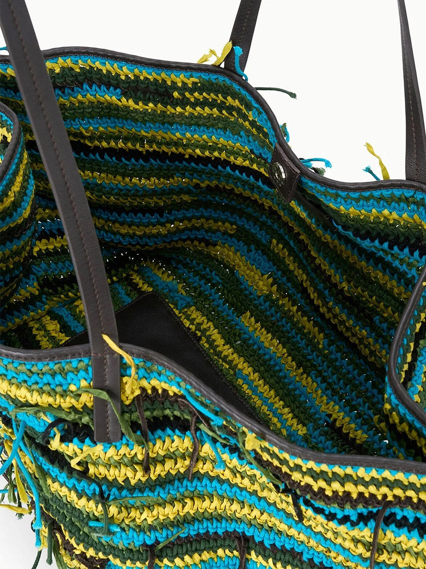 A close-up of the STAUD Christos Large Tote in Happy Sack, an open handcrafted bag with green, blue, yellow, and black stripes, dark handles, and a partially visible inner pocket.