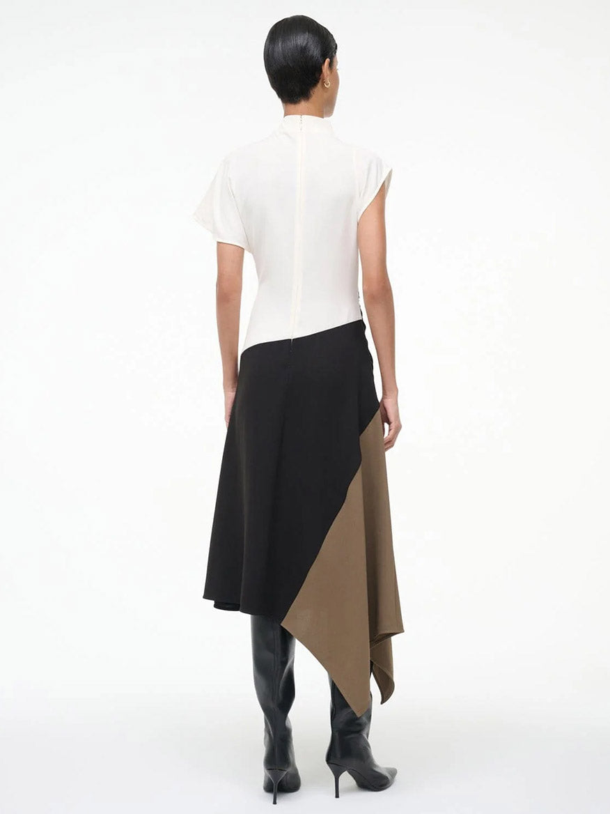 A person stands facing away, wearing the STAUD Davina Dress in Black Multi with a handkerchief hem, and black knee-high boots against a plain white background.