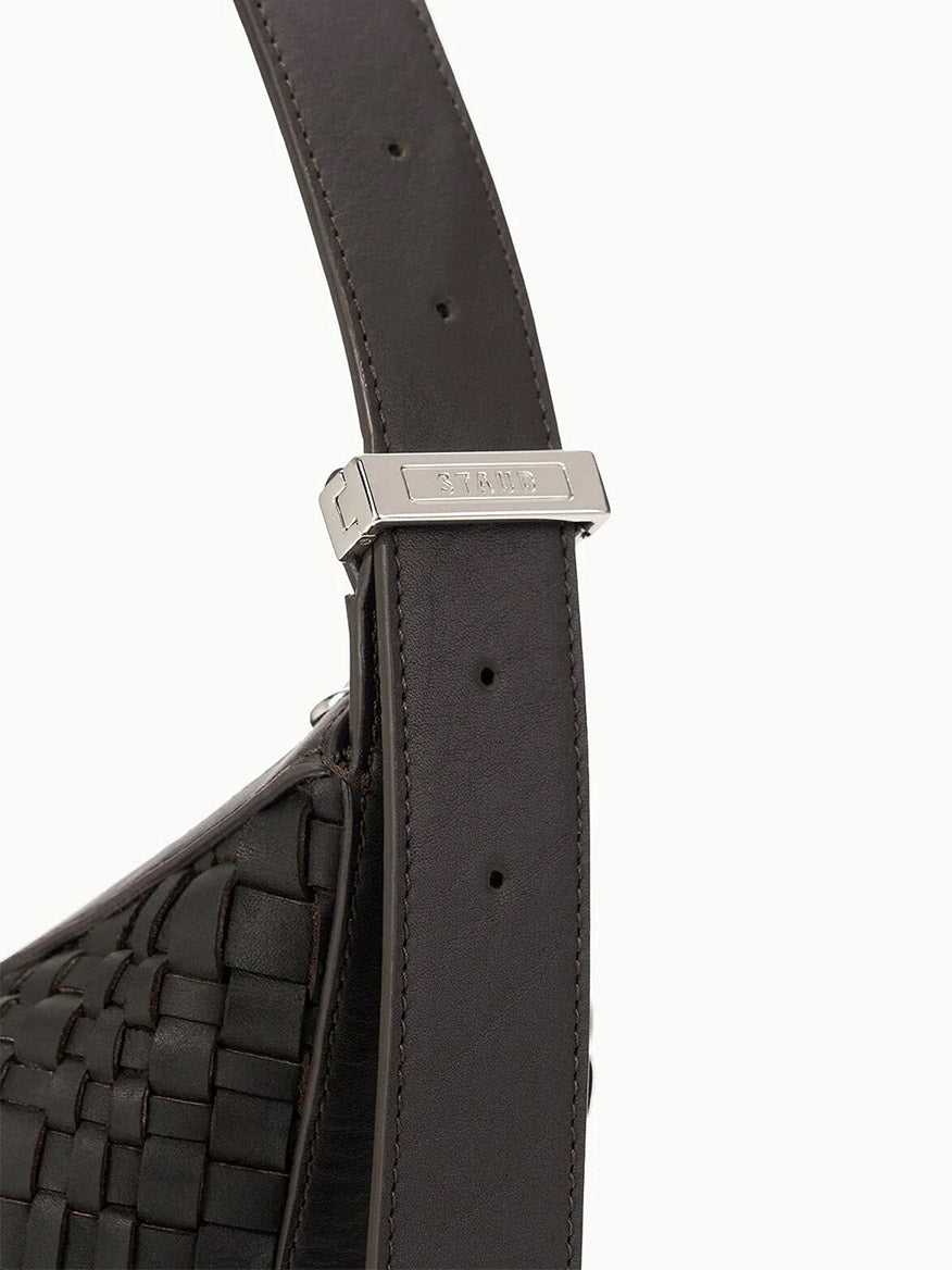 Close-up of the dark woven leather adjustable-length shoulder strap from the STAUD Large Demy Shoulder Bag in Espresso, featuring a silver rectangular buckle engraved with "STRATH".