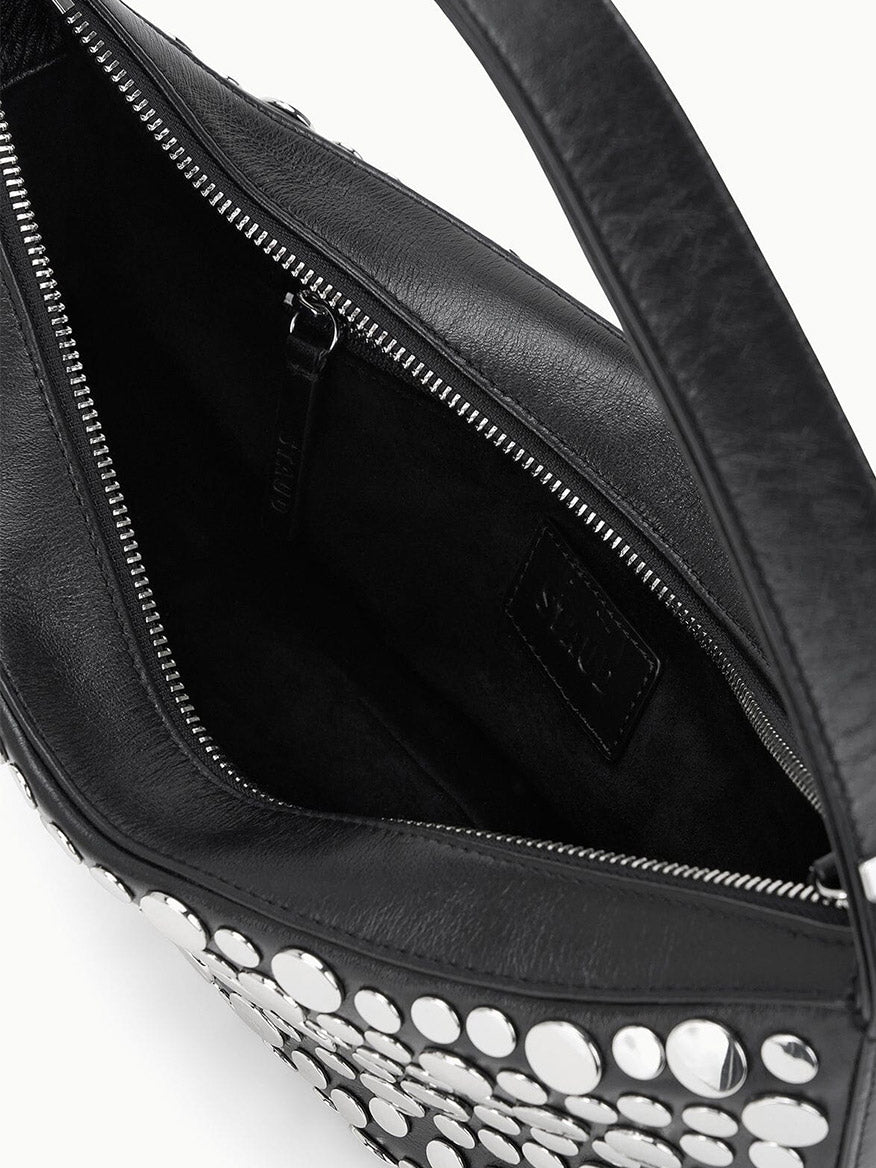 Close-up of an open STAUD Demy Shoulder Bag in Rivets, crafted from black nappa leather with silver studs, displaying the interior zippered pocket and fabric lining.