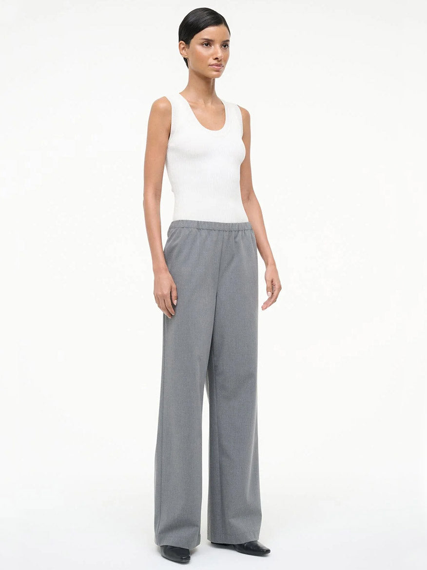 A person stands against a plain background wearing a white sleeveless top, black shoes, and loose-fitting STAUD Denali Pant in Static.