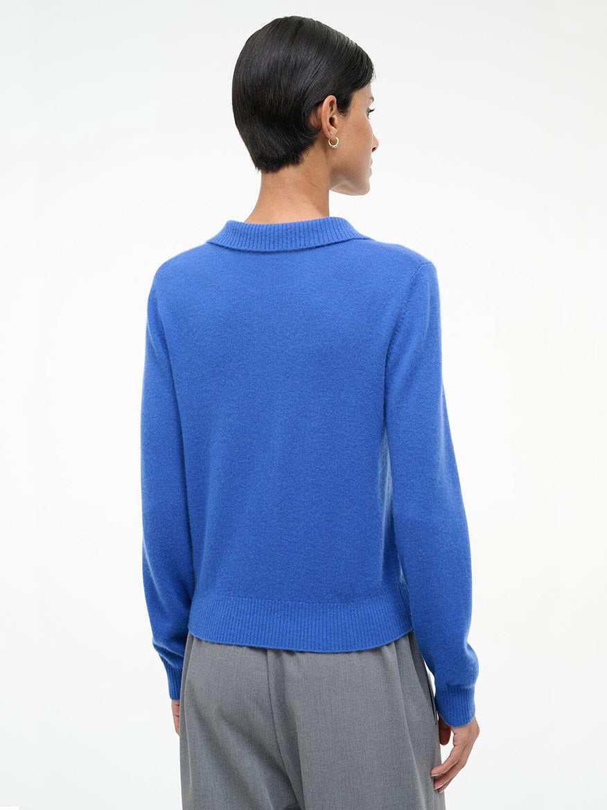 A person with short dark hair, seen from behind, wears the STAUD Gemma Cashmere Sweater in Sapphire and gray trousers against a plain white background.