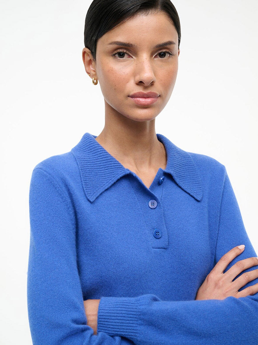 Woman with straight dark hair wearing a STAUD Gemma Cashmere Sweater in Sapphire, standing against a plain light background with her arms crossed.