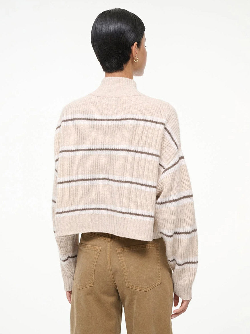 A person with short dark hair is seen from the back against a plain white background, wearing tan pants and the STAUD Hampton Cropped Cashmere Sweater in Whisper Stripe.