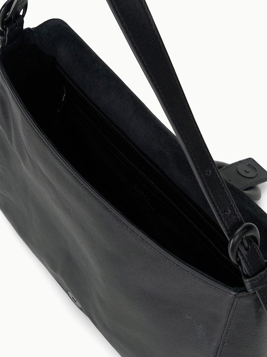 A close-up of the STAUD Harlow Medium Bag in Black showcases its leather exterior, Moon buckle, visible interior compartment, and chic shoulder strap.