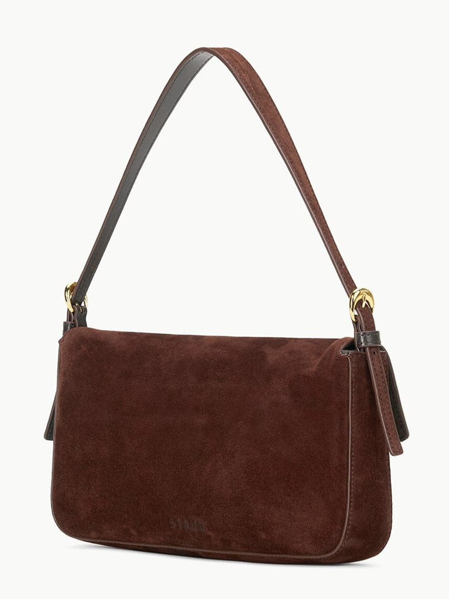 The STAUD Harlow Bag in Mahogany Suede is a brown suede shoulder bag with a short strap, gold hardware, and a signature moon buckle, shown on a plain light background.