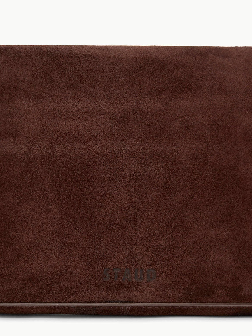 A close-up of the STAUD Harlow Bag in Mahogany Suede, featuring the brand name embossed near the bottom center and showcasing signature chic details.