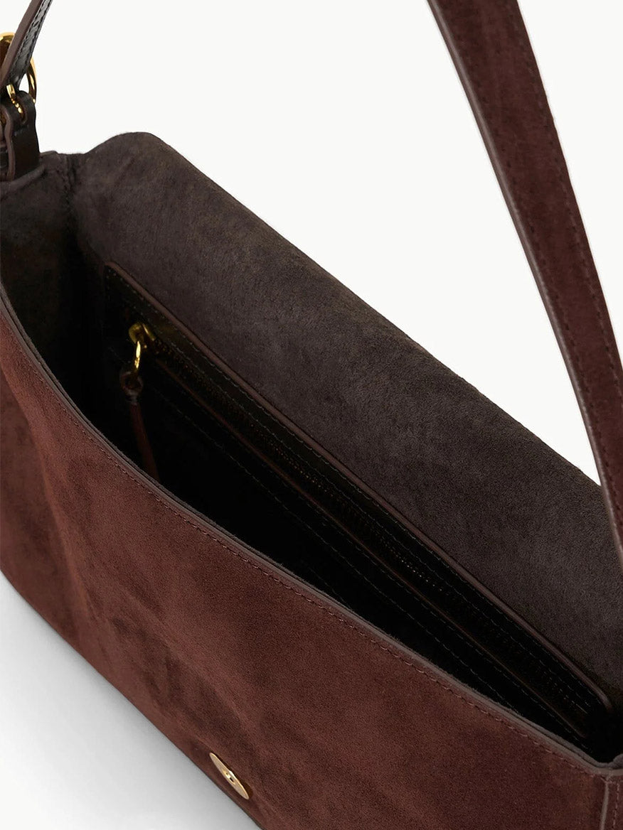Close-up of the STAUD Harlow Bag in Mahogany Suede, a brown suede shoulder bag with dark interior, inner zippered pocket, and signature moon buckle.