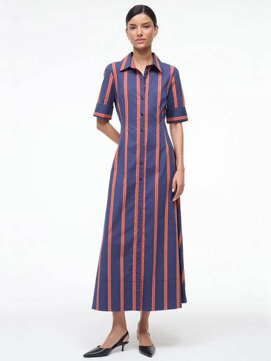 A woman wears the STAUD Joan Maxi Dress in Railroad Stripe, a long cotton poplin shirt dress with blue and orange vertical stripes, a collar, elbow-length sleeves, and black heeled shoes.