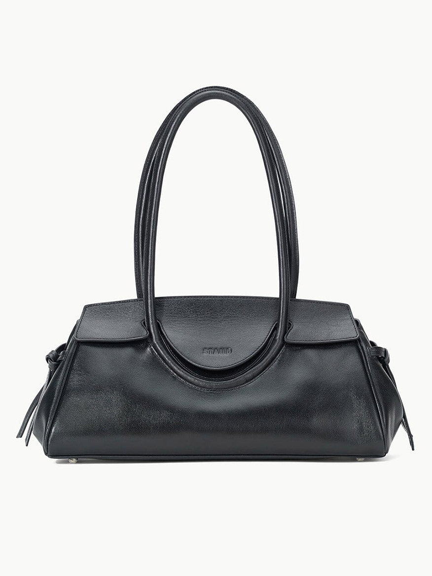 The STAUD Maude Shoulder Bag in Black is crafted from polished leather with double rounded handles and a flap closure, showcasing an elegant east-west silhouette against a plain white background.