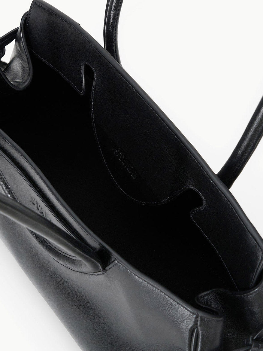 The STAUD Maude Shoulder Bag in Black features polished leather, an east-west shape, two handles, a roomy interior, and a pocket, showcased on a plain white background.