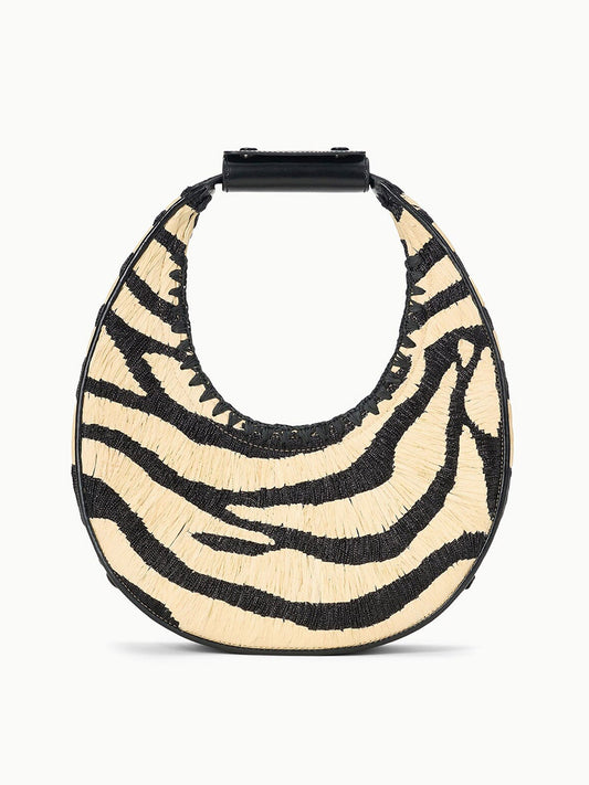 The STAUD Moon Raffia Tote Bag in Zebra features a round shape, black top handle, and a black/natural zebra-patterned raffia design.