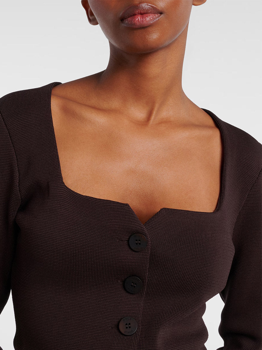 Someone wearing the STAUD Rachela Sweater in Earth—a dark brown, long-sleeve knit top with a notched square neck and three black buttons down the front.
