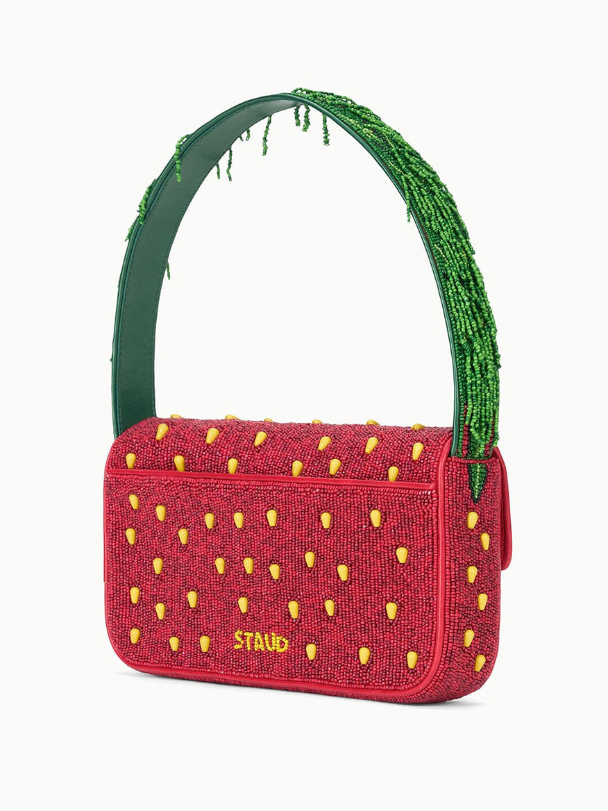 The STAUD Tommy Beaded Bag in Strawberry Dream features a red beaded body with yellow seed details and a green handle, playfully designed to resemble a strawberry.