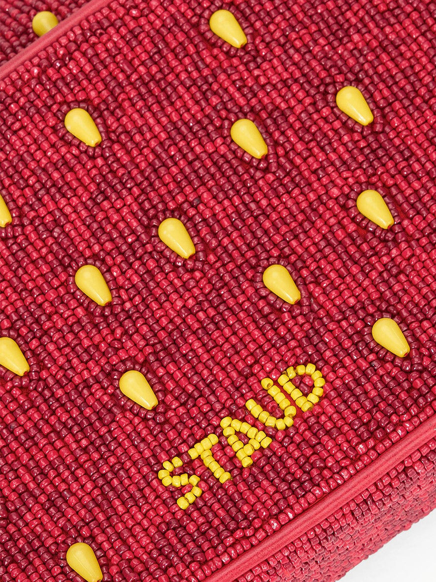 Close-up of a textured red surface with small yellow teardrop shapes and "STAUD" in yellow beads, inspired by the STAUD Tommy Beaded Bag in Strawberry Dream.