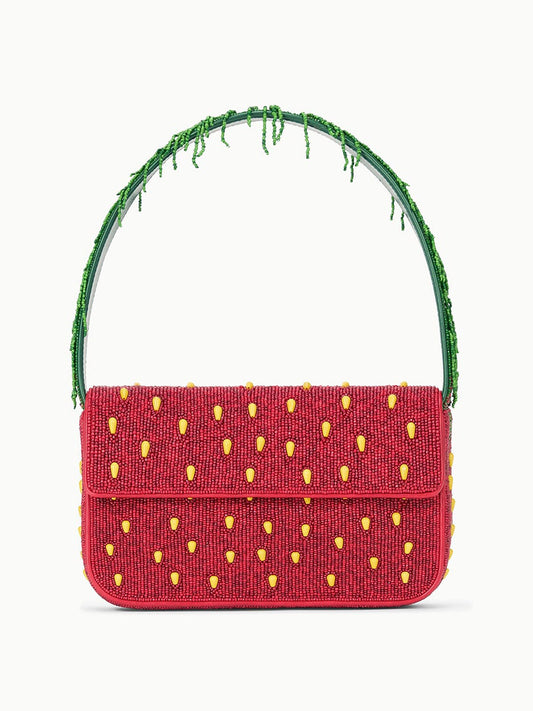 The STAUD Tommy Beaded Bag in Strawberry Dream is a rectangular red shoulder bag with yellow accents, a green beaded handle, and a playful strawberry pattern.