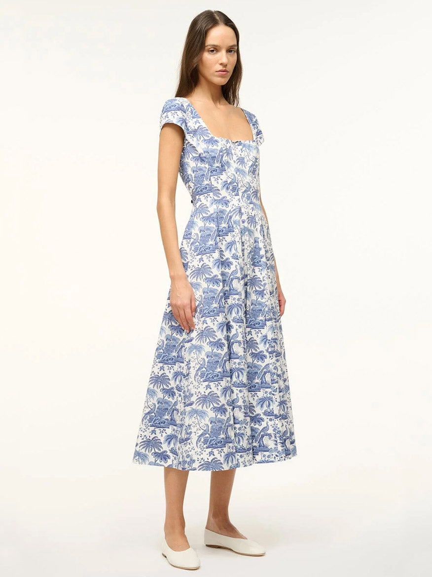 A woman wears the STAUD Wells Short Sleeve Dress in Blue Toile, featuring an A-line skirt and corset-style paneling, paired with white flats against a plain light background.
