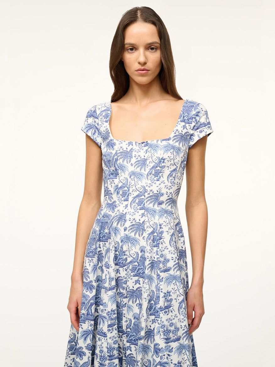 Woman wearing the STAUD Wells Short Sleeve Dress in Blue Toile, featuring blue and white floral print, short sleeves, and an a-line midi silhouette, standing against a plain light background.
