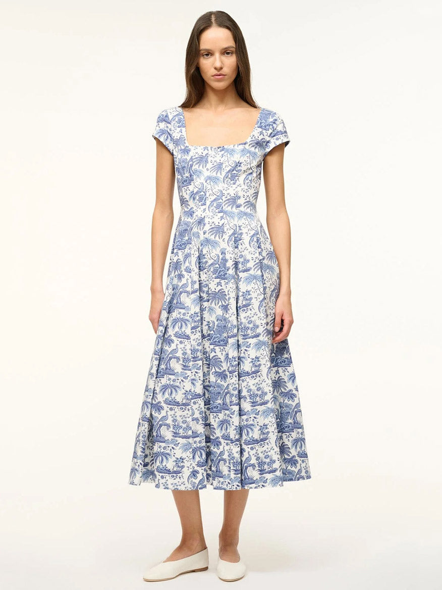 Woman wearing the STAUD Wells Short Sleeve Dress in Blue Toile, featuring a blue and white pattern, short sleeves, square neckline, and corset-style panel, standing against a plain light background.