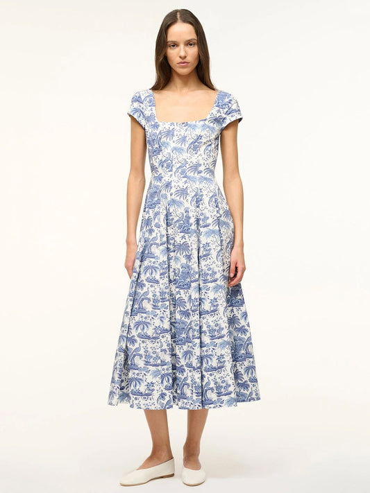 Woman wearing the STAUD Wells Short Sleeve Dress in Blue Toile, featuring a blue and white pattern, short sleeves, square neckline, and corset-style panel, standing against a plain light background.