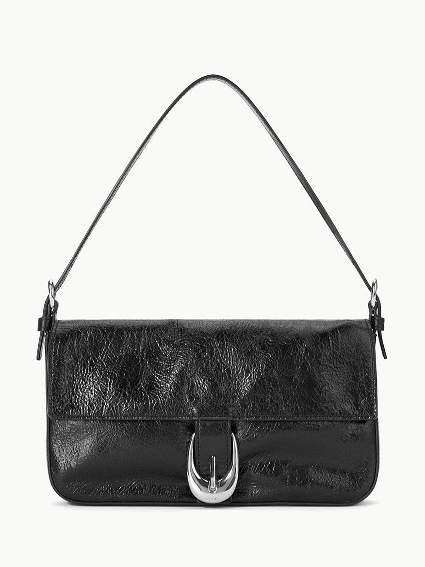 The STAUD Harlow Bag in Black is a crinkle leather shoulder bag featuring a short strap and a large silver buckle on the front flap, shown against a plain white background.