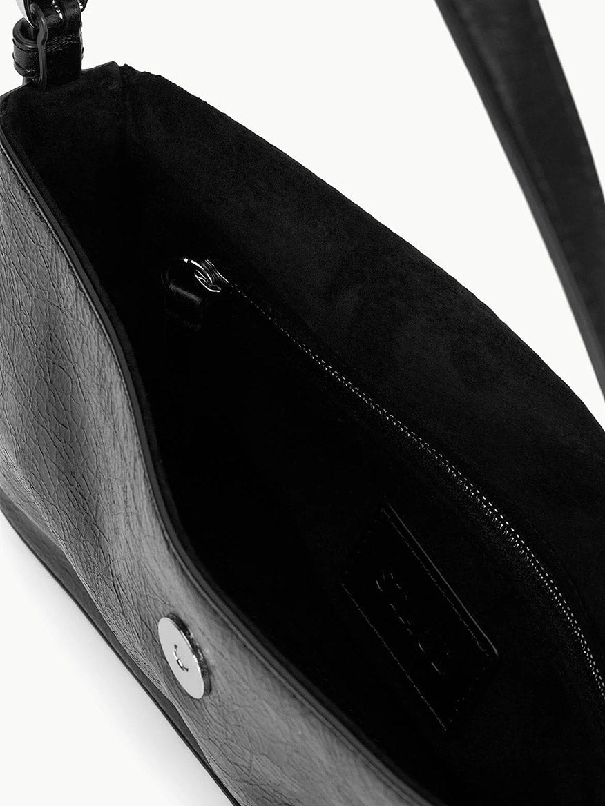A close-up of the STAUD Harlow Bag in Black reveals its crinkle leather interior with a zippered pocket and a magnetic snap closure.